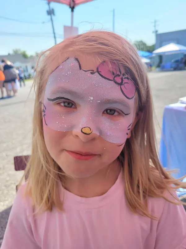 Child with a pink kitty face paint design with a bow