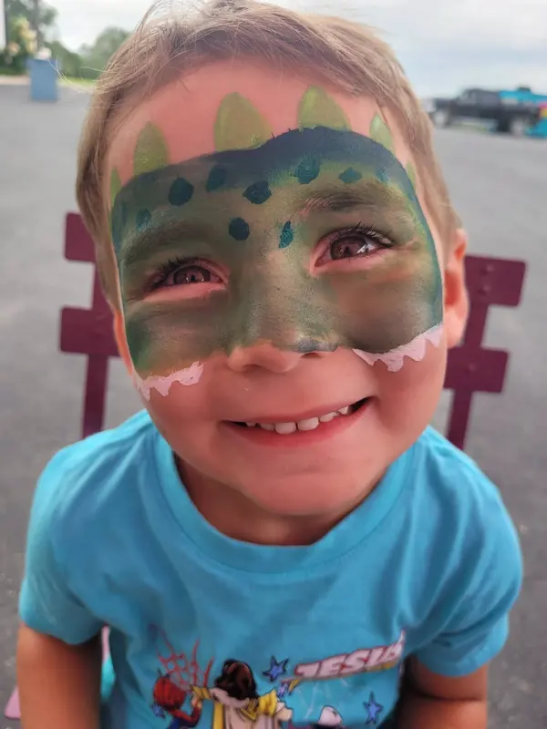 Child with a green dinosaur face paint design