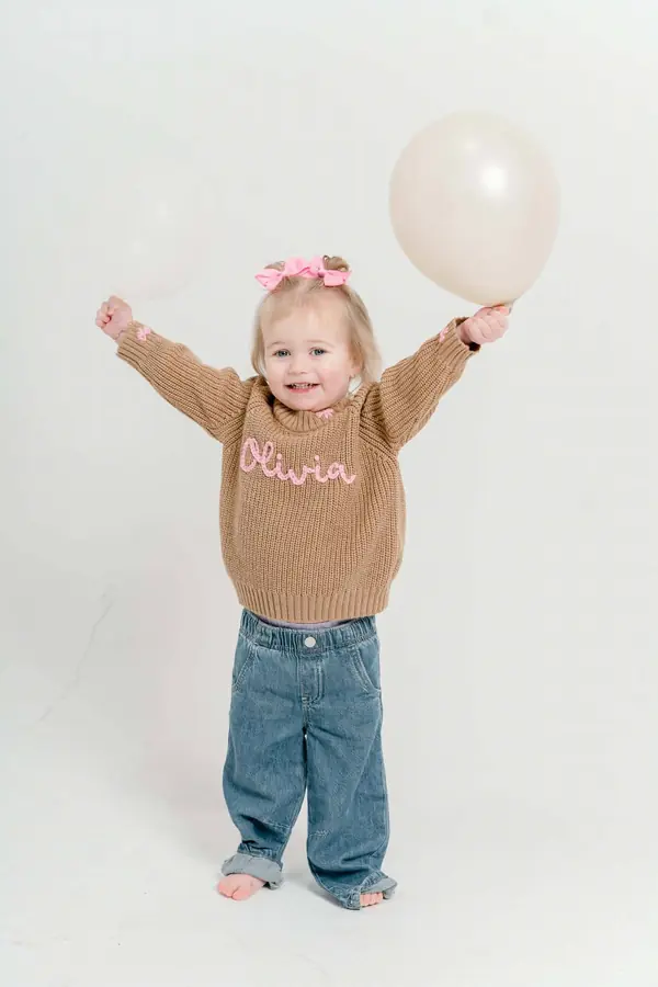 Toddler holding a balloon in a name-embroidered sweater