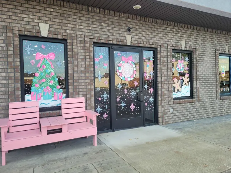 Pastel Christmas windows on a storefront with a pink bench