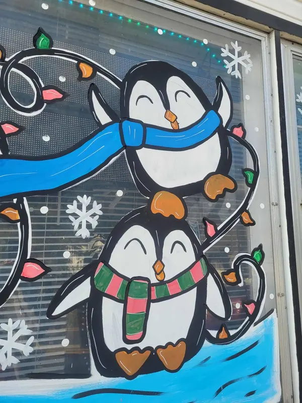 Window painted with two penguins in scarves and holiday lights
